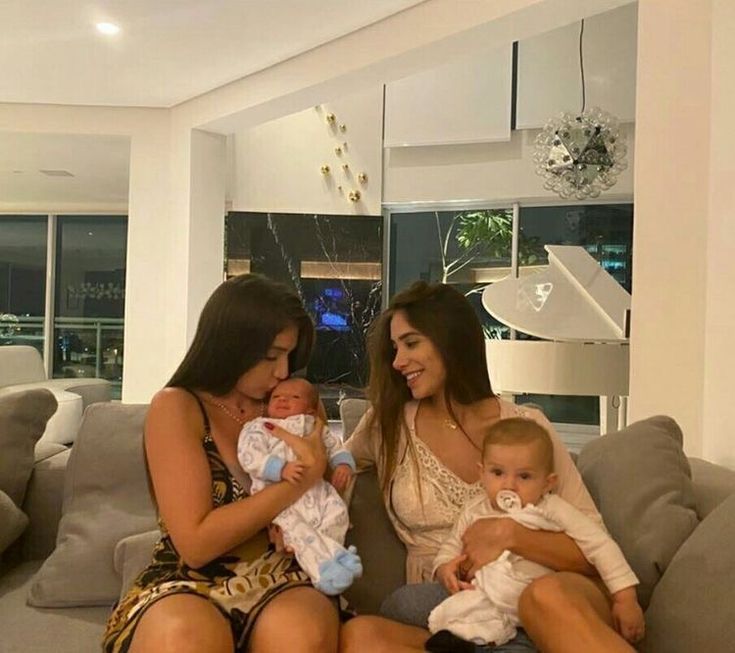 two women sitting on a couch with a baby in her lap and another woman holding a baby