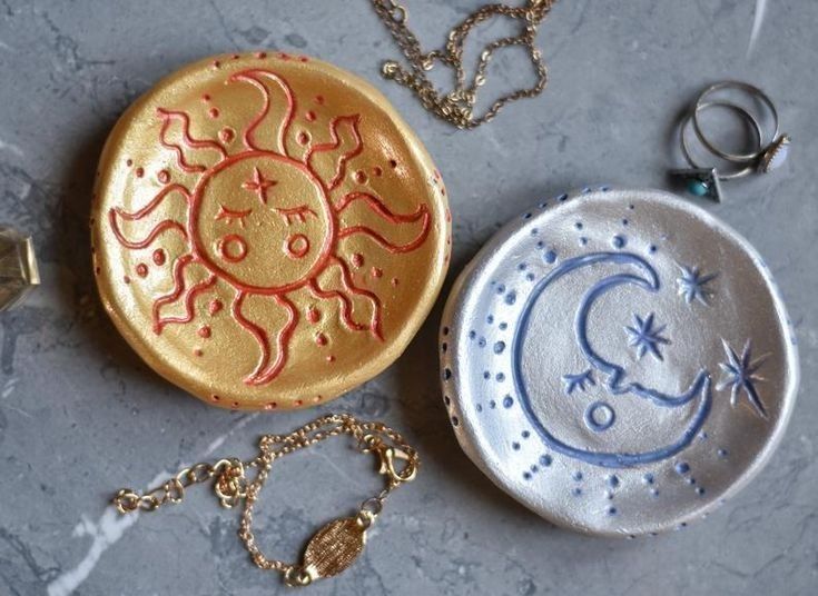 two ceramic dishes sitting on top of a table next to necklaces and ring holders