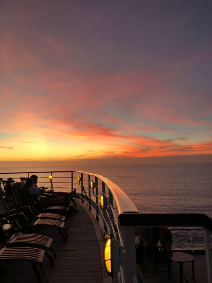 people are sitting on the deck of a cruise ship watching the sun set over the ocean