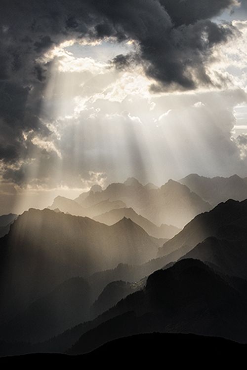 the sun shines through dark clouds over mountains