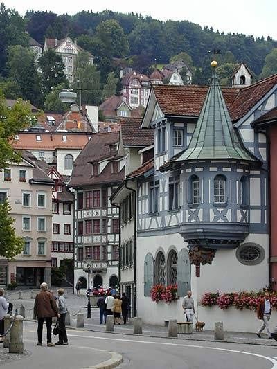 people are walking down the street in front of some buildings with flowers growing on them