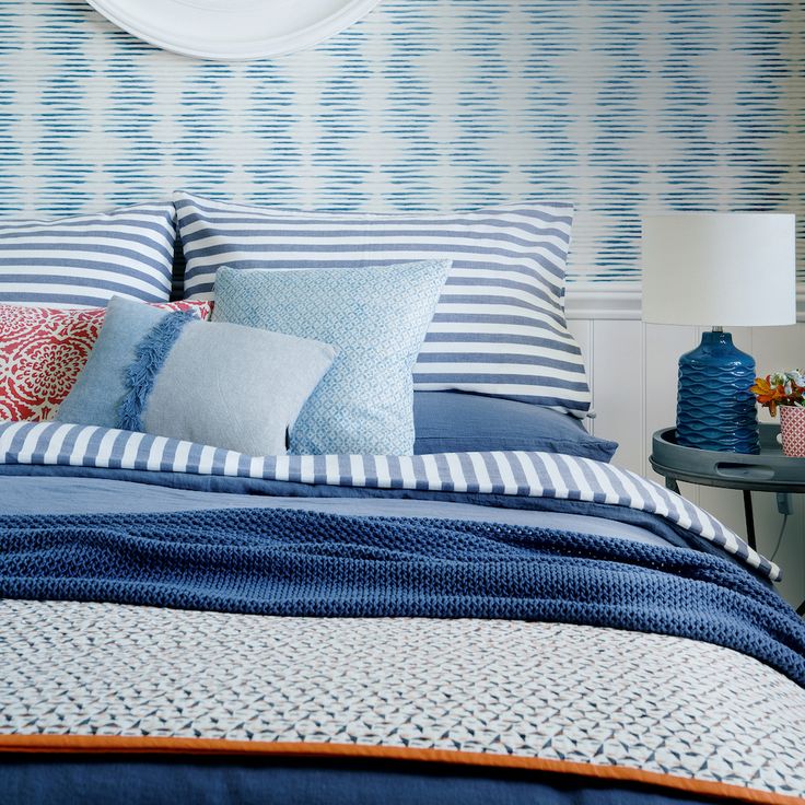 a bed with blue and white striped pillows on it's headboard next to a night stand