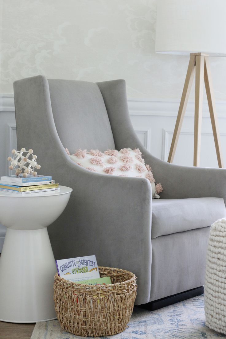 a gray chair sitting next to a white table with a basket on top of it