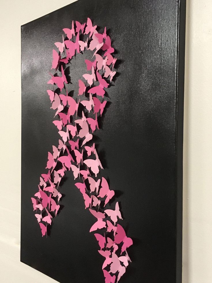 a pink ribbon made out of paper butterflies on a black background with white wall behind it