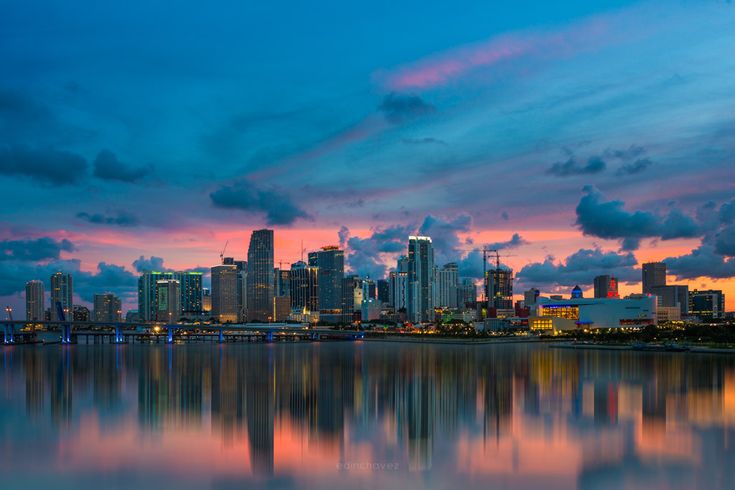 the city skyline is reflected in the water at sunset or dawn with clouds and blue sky