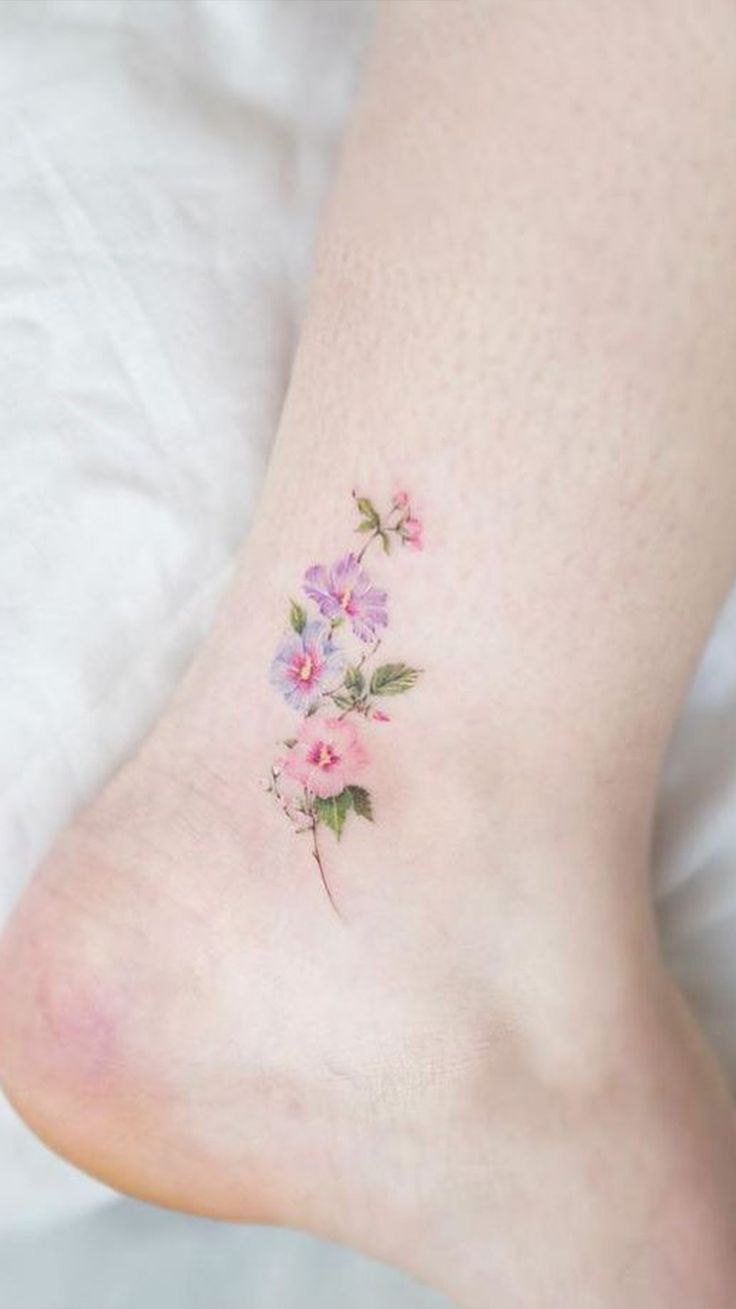 a small flower tattoo on the foot of a woman's left leg, with pink flowers and green leaves