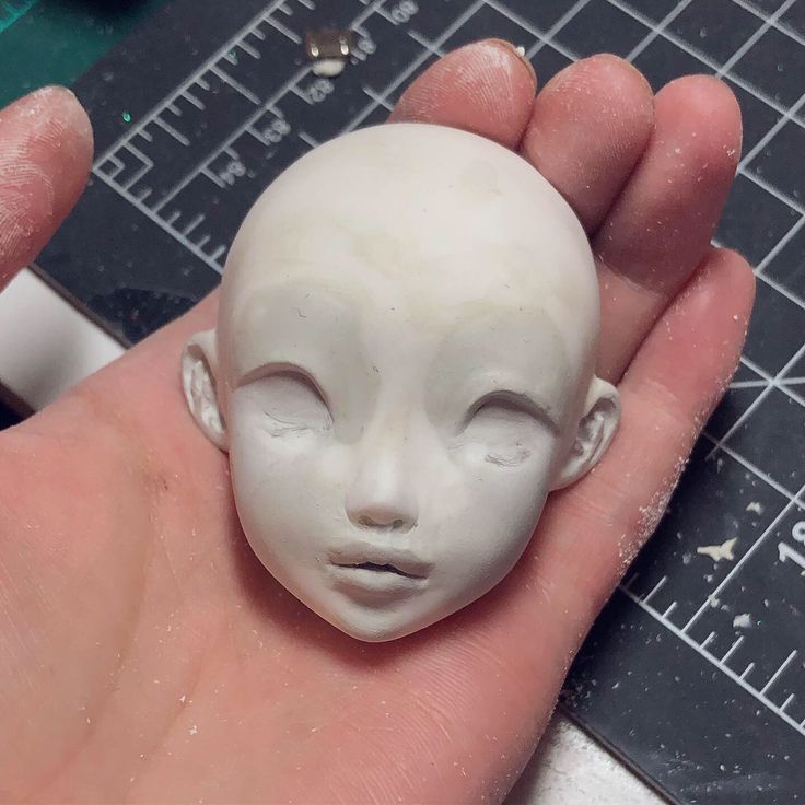 a hand holding a small white ceramic face