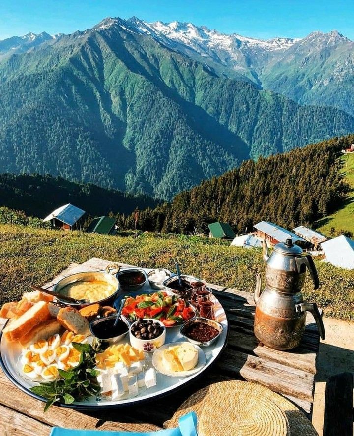 an outdoor table with food on it in the mountains