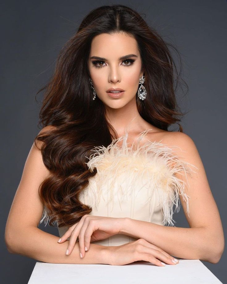 a woman with long dark hair wearing a white dress and feathered shawl over her shoulder