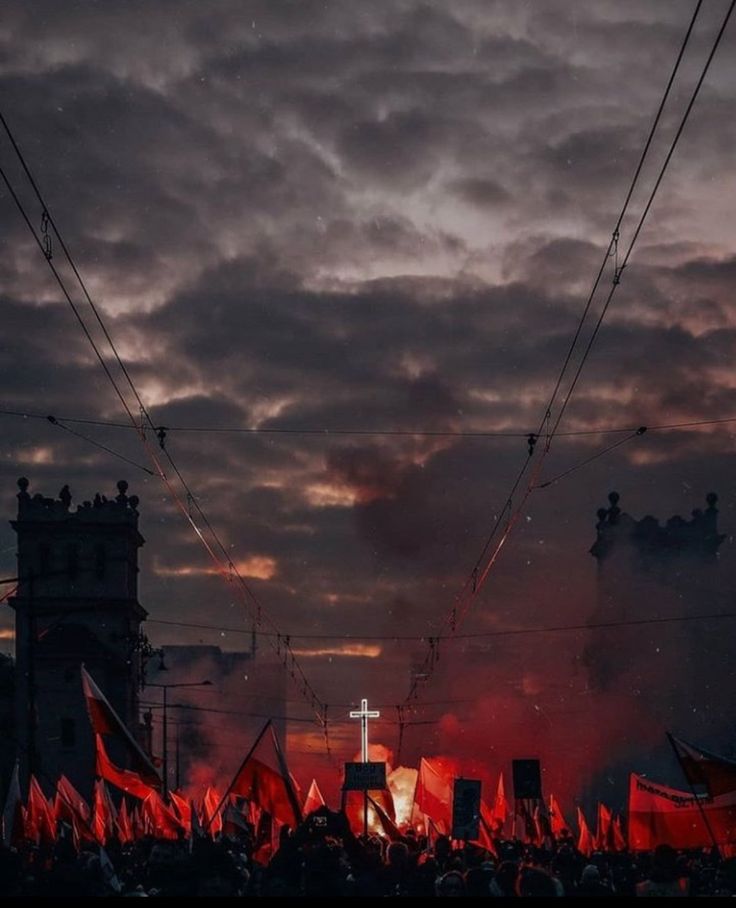 a group of people holding red flags in front of some buildings and clouds at night