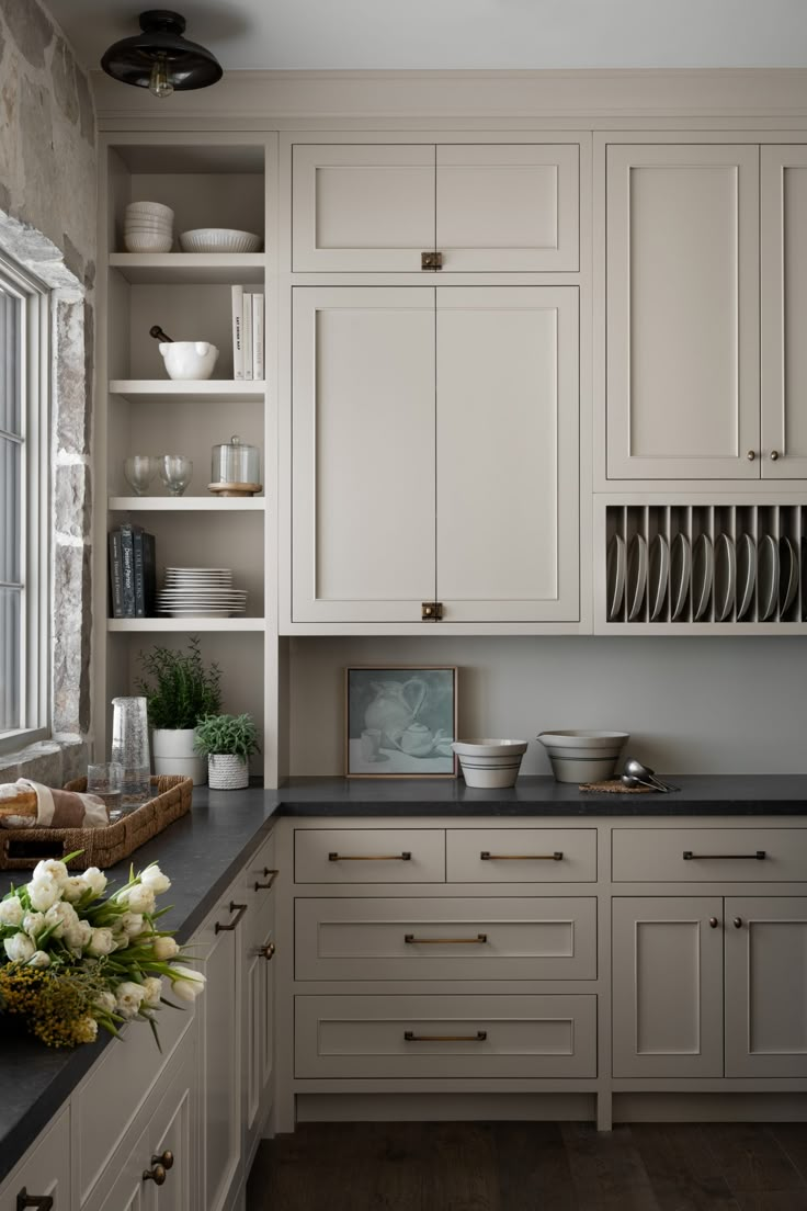 a kitchen with lots of white cabinets and black counter tops, flowers in the middle