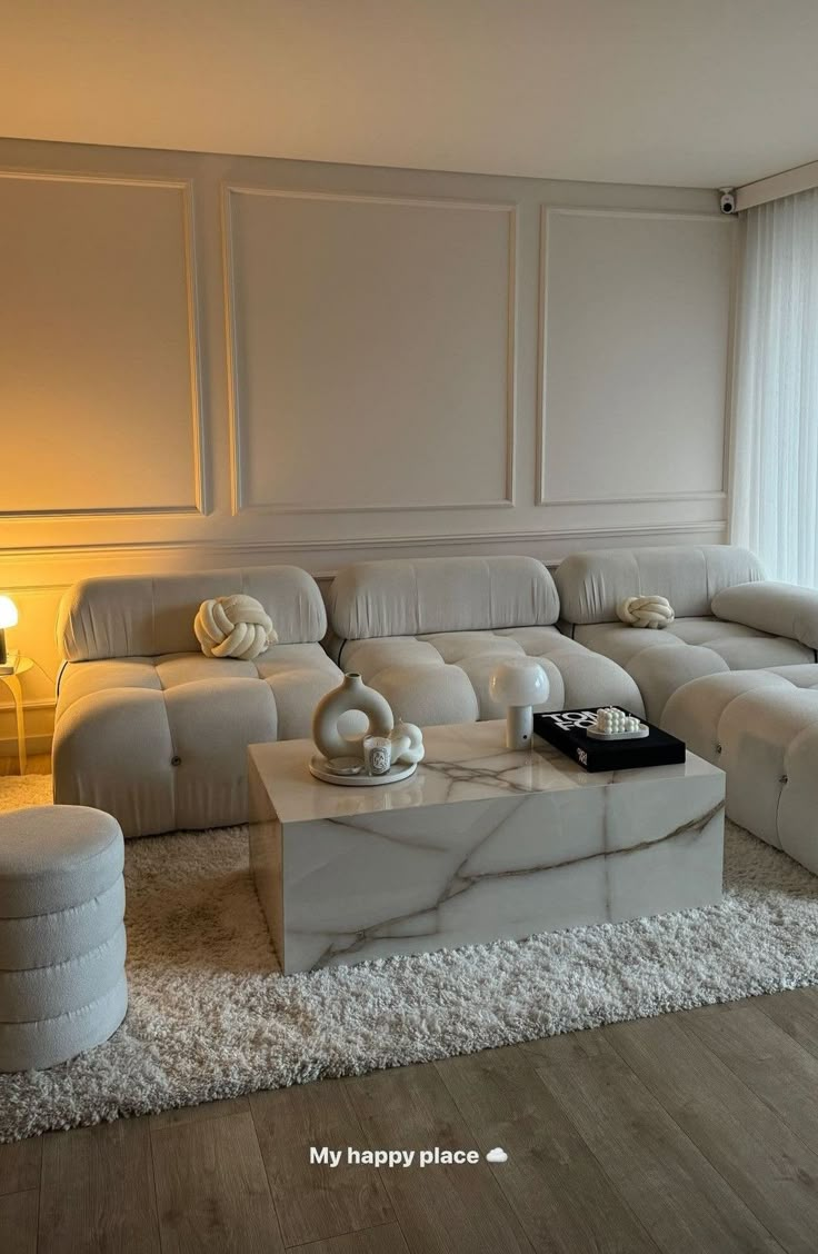 a living room filled with white furniture next to a large window and a rug on the floor