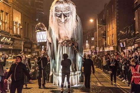 a group of people standing on the side of a street next to a giant statue