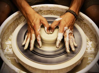 two hands on a wheel making something out of clay