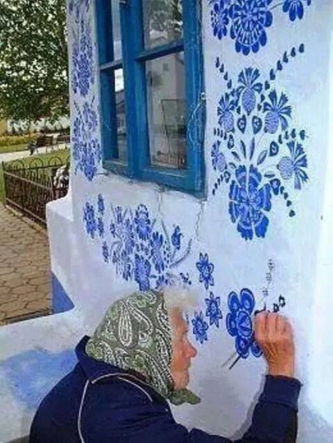 a man painting the side of a building with blue and white flowers on it's wall