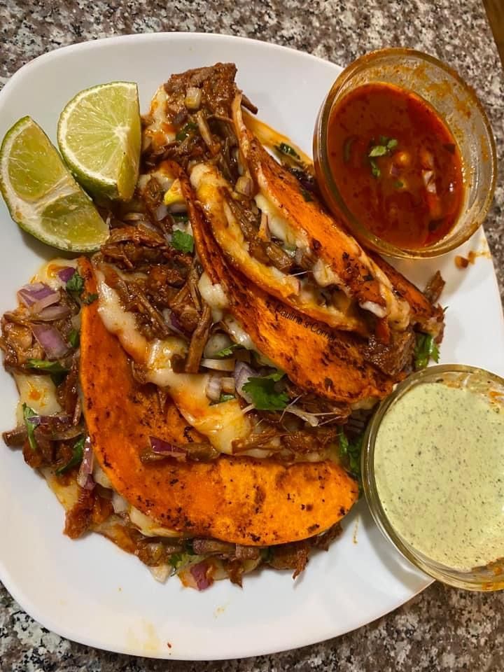 a white plate topped with tacos and sauces next to a bowl of salsa