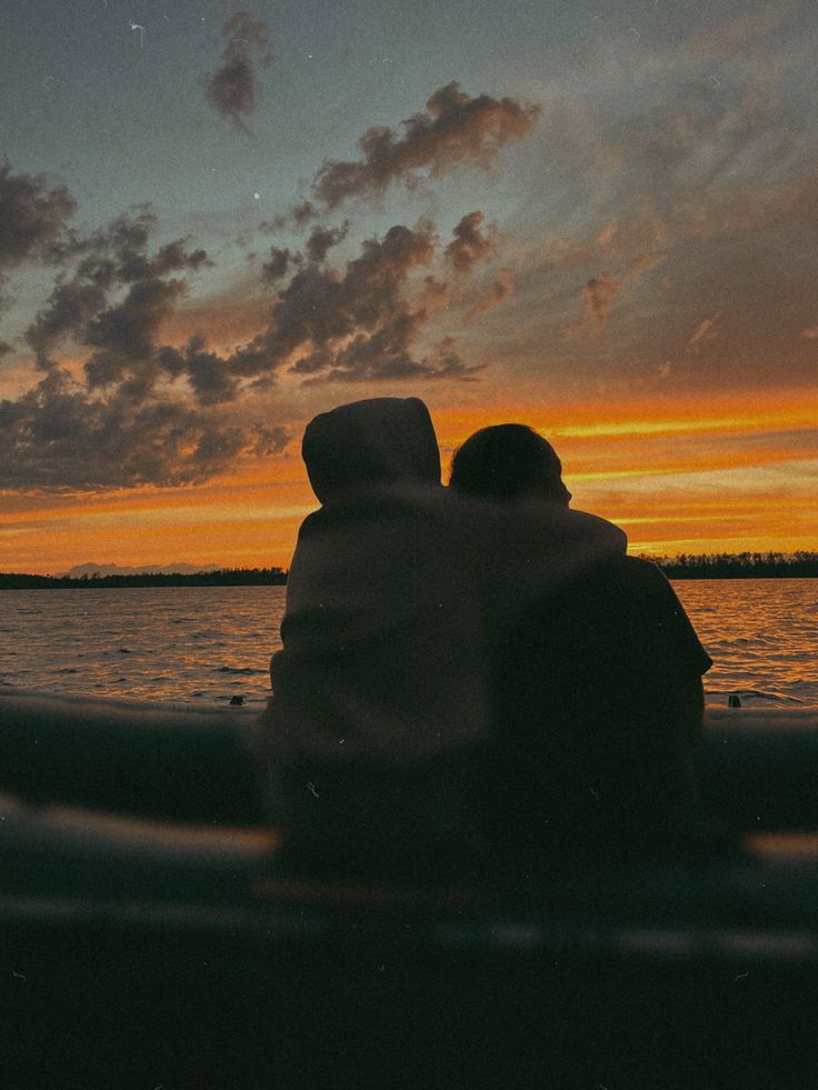 two people sitting on a boat watching the sunset