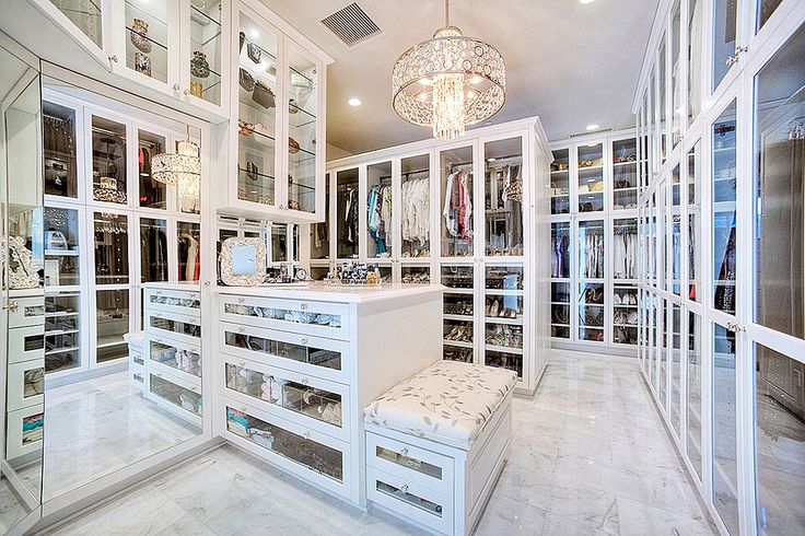 a walk in closet with lots of white drawers and glass doors on the walls, along with a chandelier hanging from the ceiling