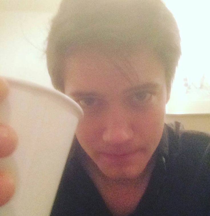 a close up of a person holding a cup in front of his face and looking at the camera