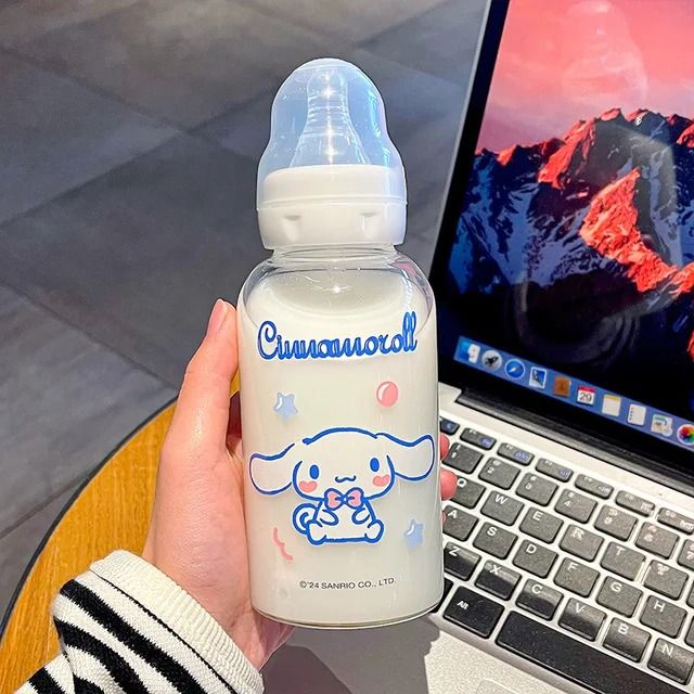 someone is holding a baby bottle in front of their laptop and the computer screen has an image of a dog on it