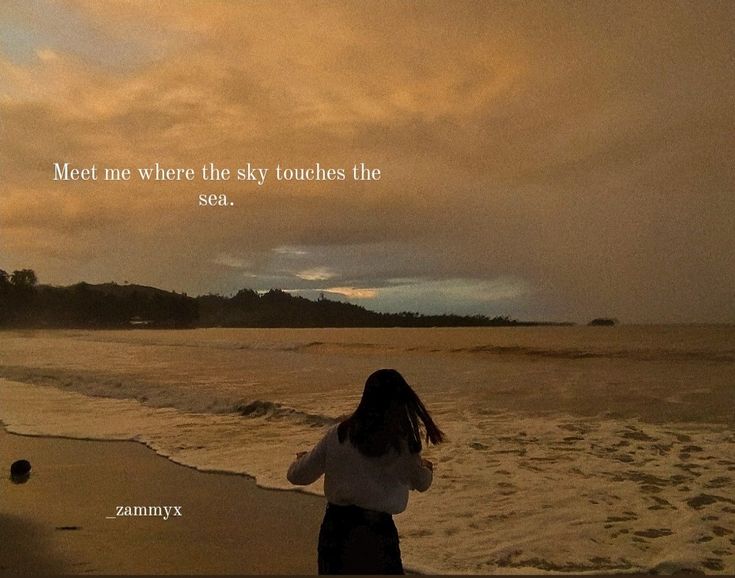 a woman standing on top of a beach next to the ocean under a cloudy sky