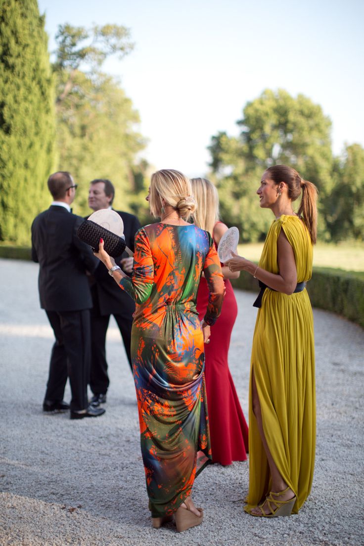 two women in long dresses talking to each other while others stand around and look on