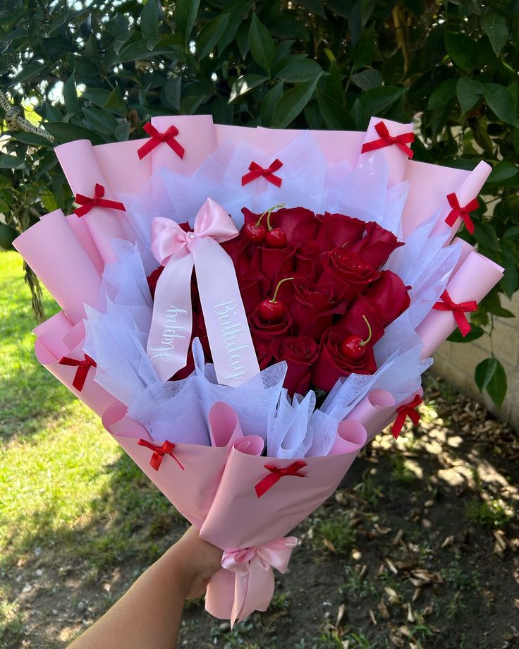 someone holding a bouquet of red roses in their hand with the ribbon tied around it