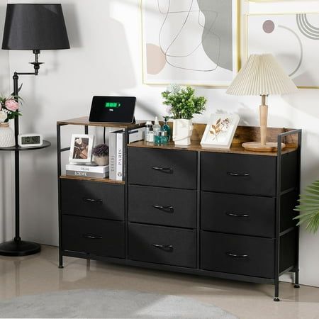 a living room with a black dresser and pictures on the wall above it, along with a lamp