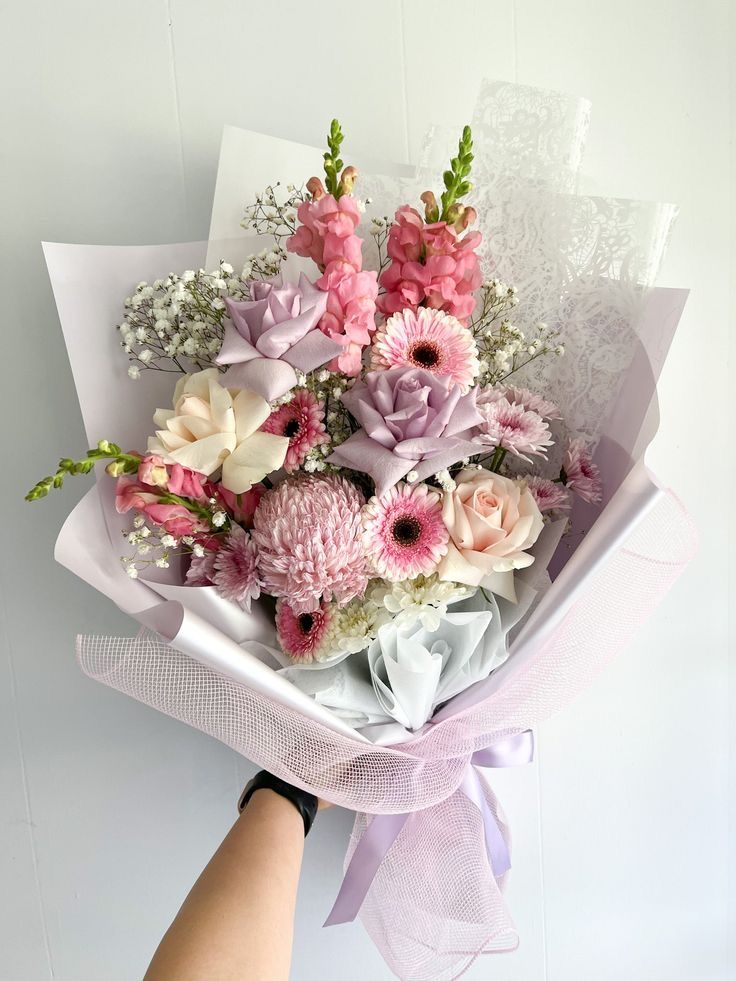 a bouquet of flowers is being held by a woman's hand in front of a white wall