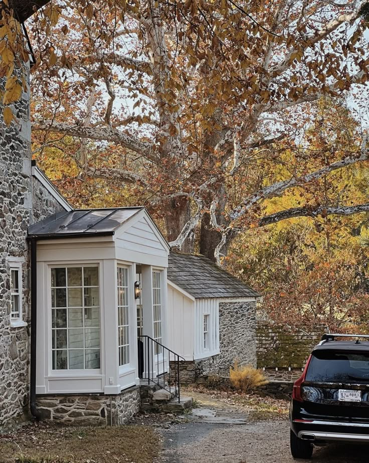 a car parked in front of a stone house with autumn leaves on the trees around it