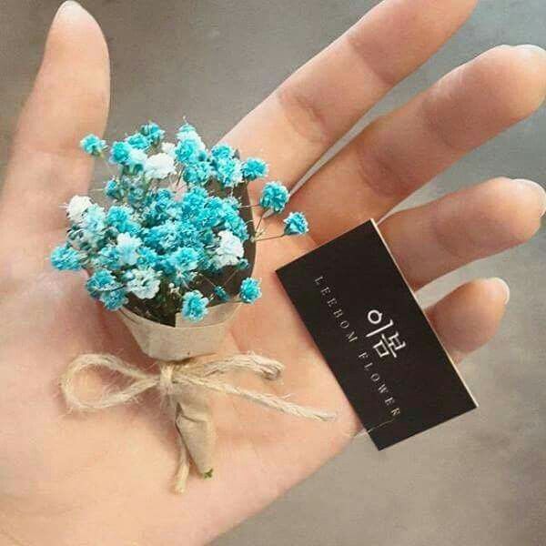 small blue flowers are in a tiny pot on someone's hand with a tag