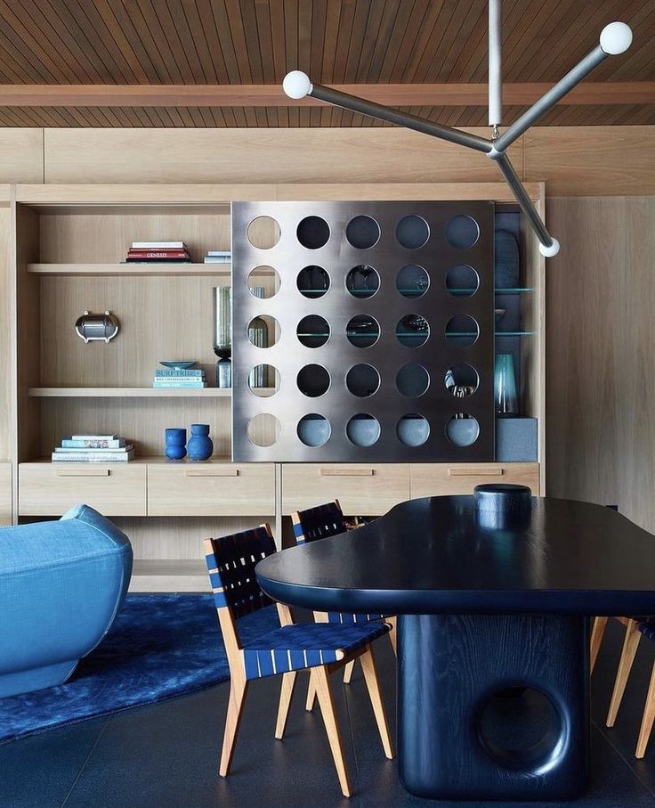 a modern dining room with blue chairs and a black table in front of a bookcase