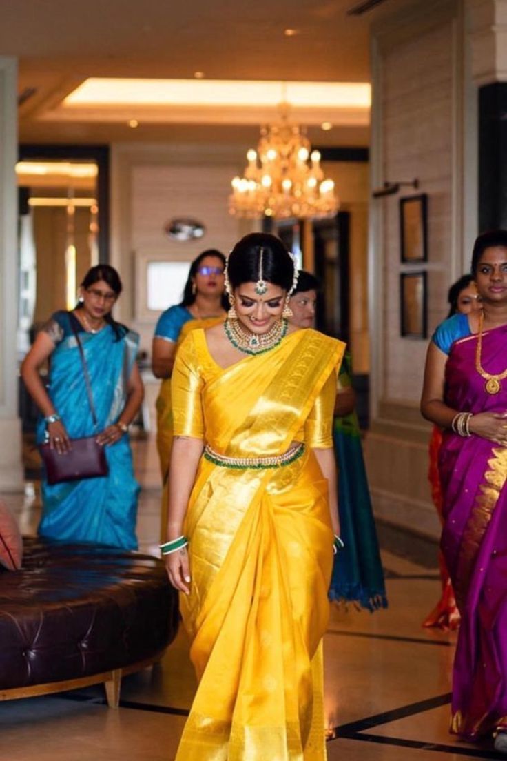 a woman in a yellow sari walking down the hall with other people behind her