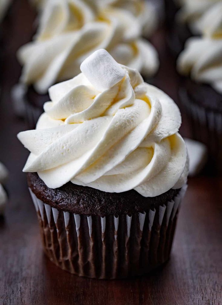 chocolate cupcakes with white frosting and sprinkles on a wooden table