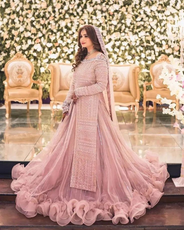 a woman in a pink gown standing next to a flower covered stage with flowers on the wall