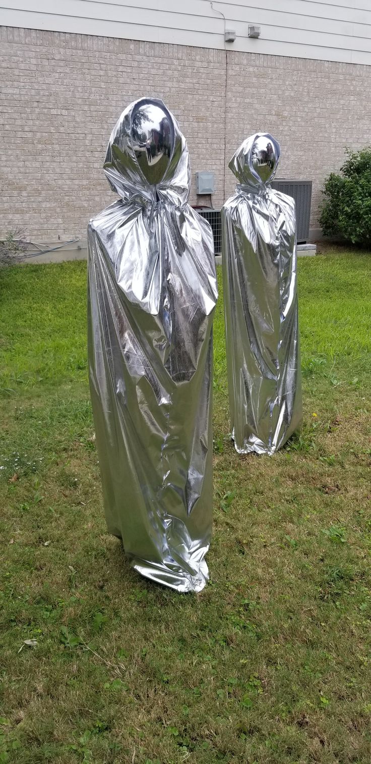 two silver statues wrapped in plastic sitting on top of a grass covered field next to a building