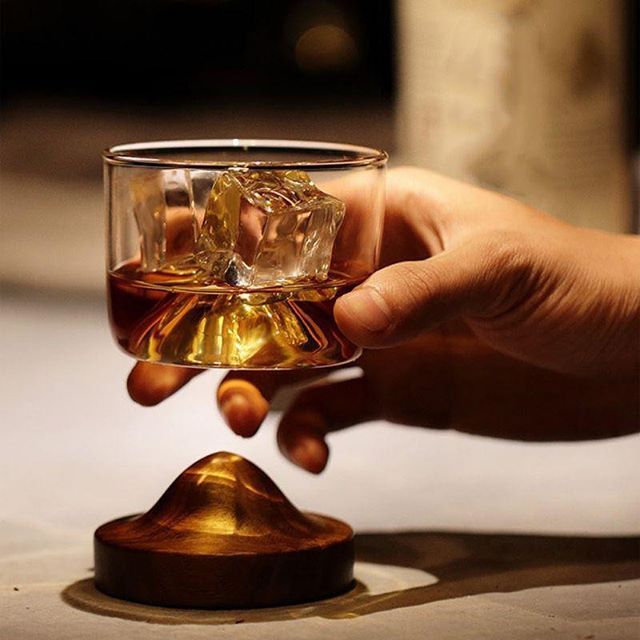 a hand holding a glass with some liquid in it and ice cubes on the rim