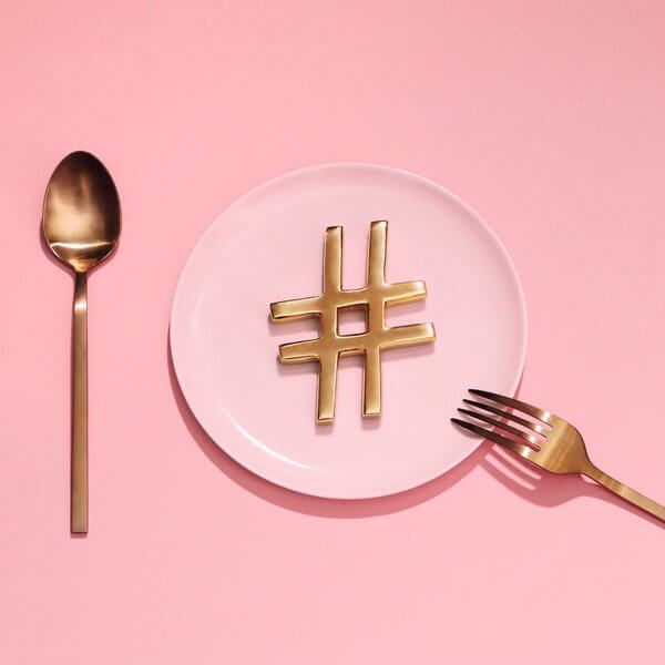 a white plate topped with a golden hash logo next to a fork and knife on a pink surface