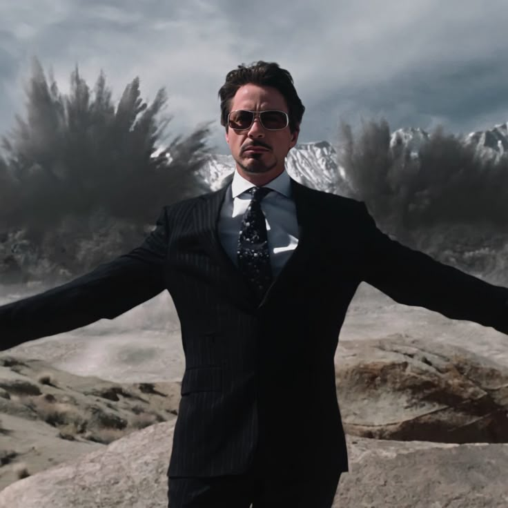 a man in a suit and sunglasses standing on rocks