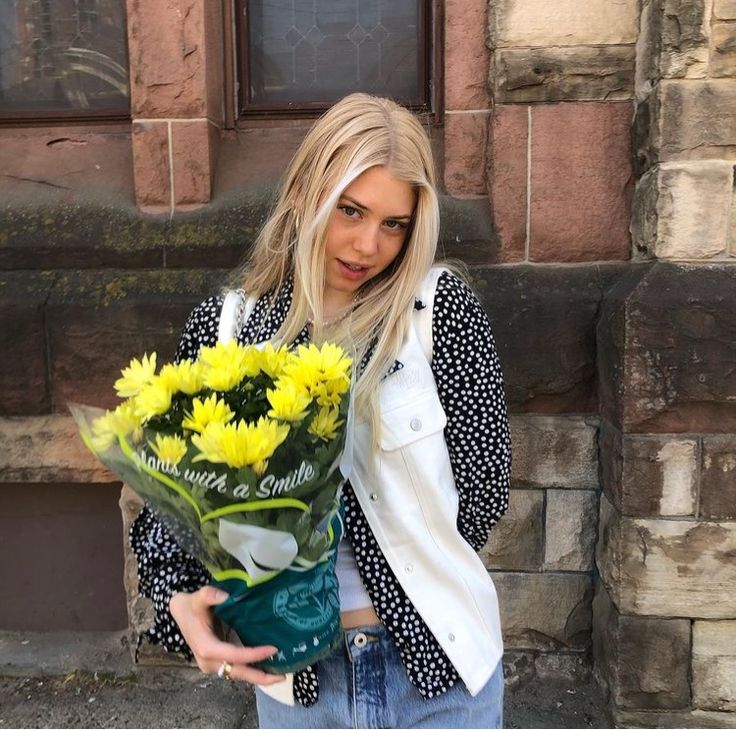 a woman holding a bouquet of yellow flowers in front of a brick wall and door