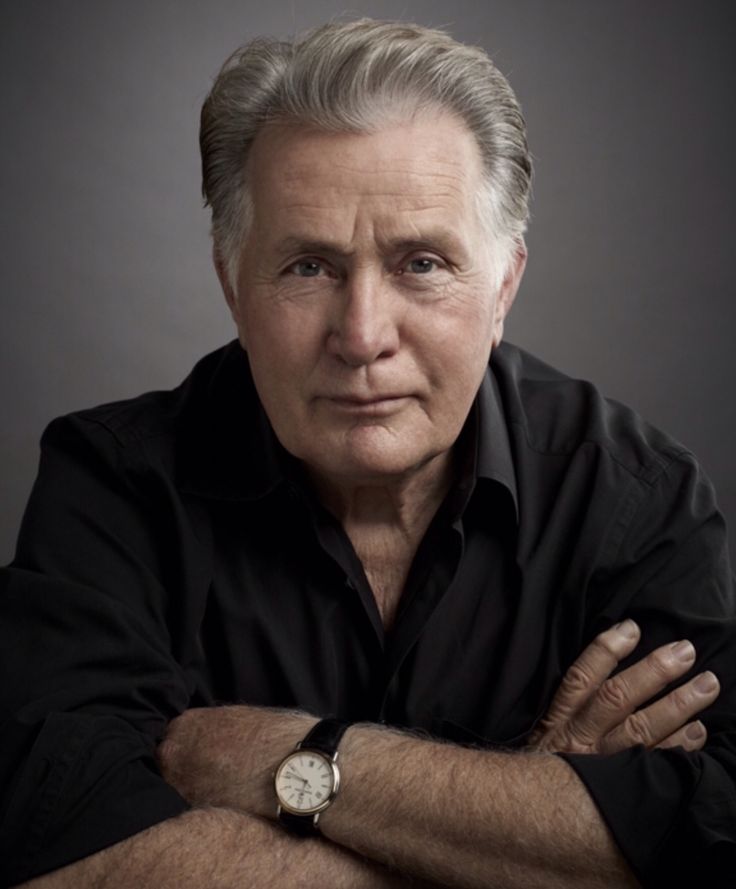 an older man with his arms crossed looking at the camera while wearing a black shirt