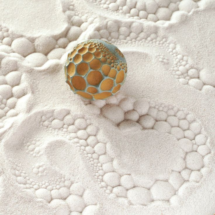 a ball sitting on top of a bed covered in white and gold circles next to a wall