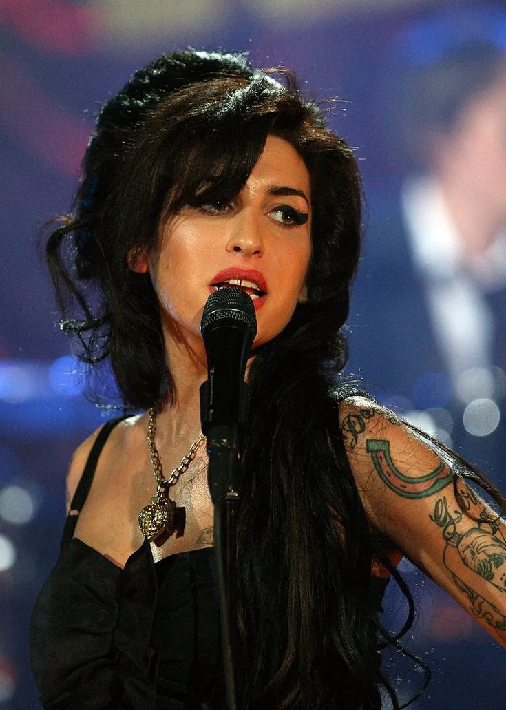 a woman with long black hair and tattoos on her arm singing in front of a microphone