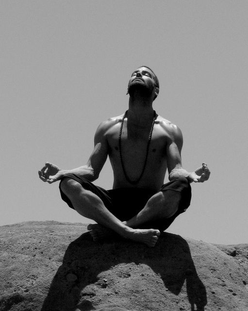 a man sitting in the middle of a yoga pose on top of a rock with his eyes closed