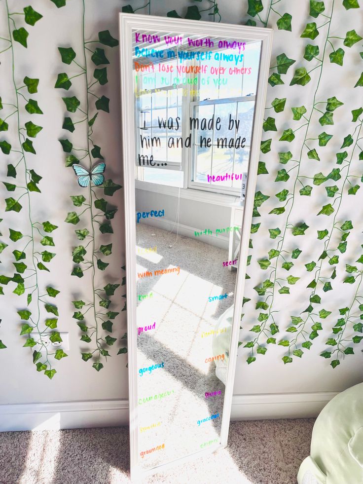 a mirror with writing on it next to a wall covered in ivy leaves and vines