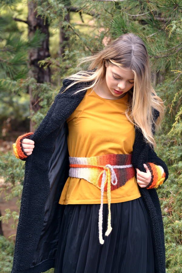 a woman in a yellow shirt and black skirt is wearing a long coat over her shoulders