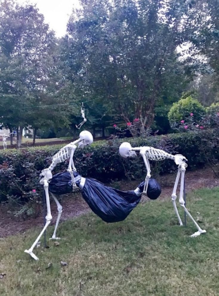 two skeleton statues are in the grass with one laying on his back and another standing behind him