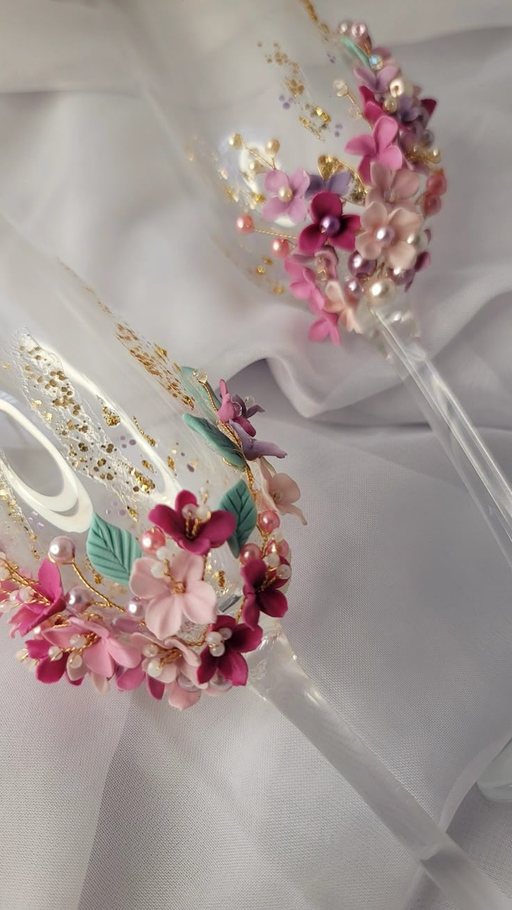 two tiaras with flowers and pearls on top of each other, sitting on a white cloth