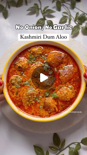 a person holding a bowl of food with the words no onion, no garlic kashmi dum aloo