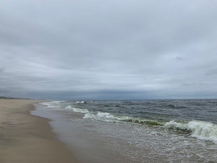 an ocean beach with waves coming in to shore and cloudy skies above the water on a gray, overcast day